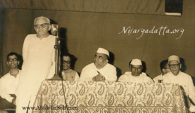 Frydman speaking at a function in Bombay. Nisdargadatta Maharaj is sitting second from the right.