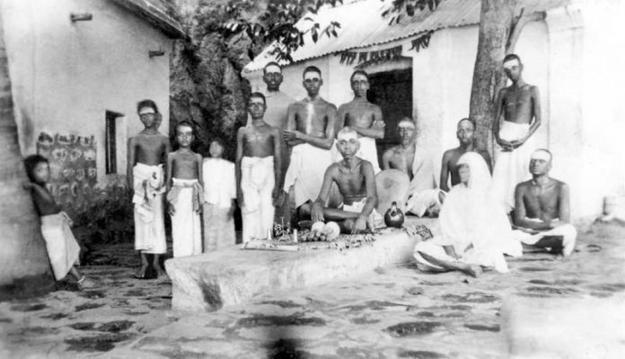 Bhagavan and his mother sitting in courtyard of Skandashram. Kunju Swami is sitting on the right
