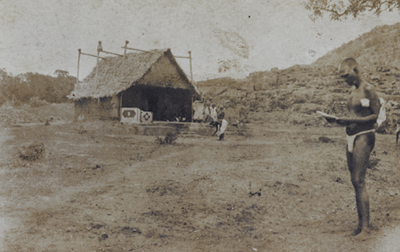 The first thatched building that was built over the Mother's Samadhi. Bhagavan is on the right, reading a letter.